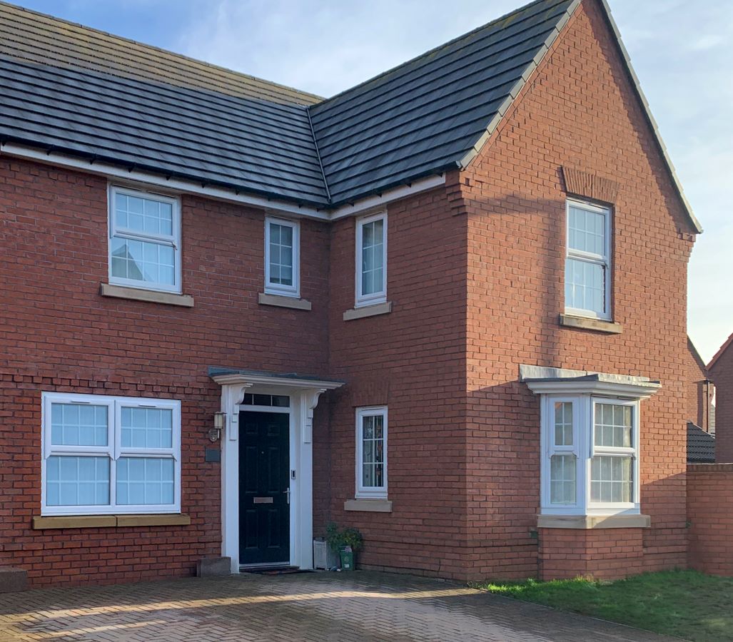 front of red brick house showing white upvc windows and dark front door in the shade